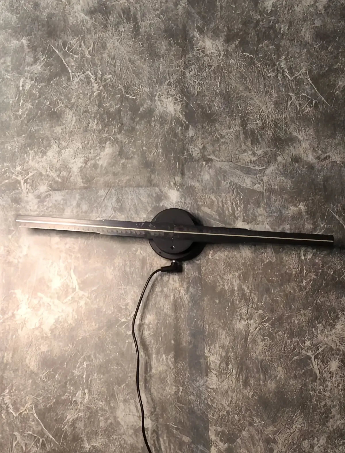 Black holographic fan display mounted on a gray textured wall