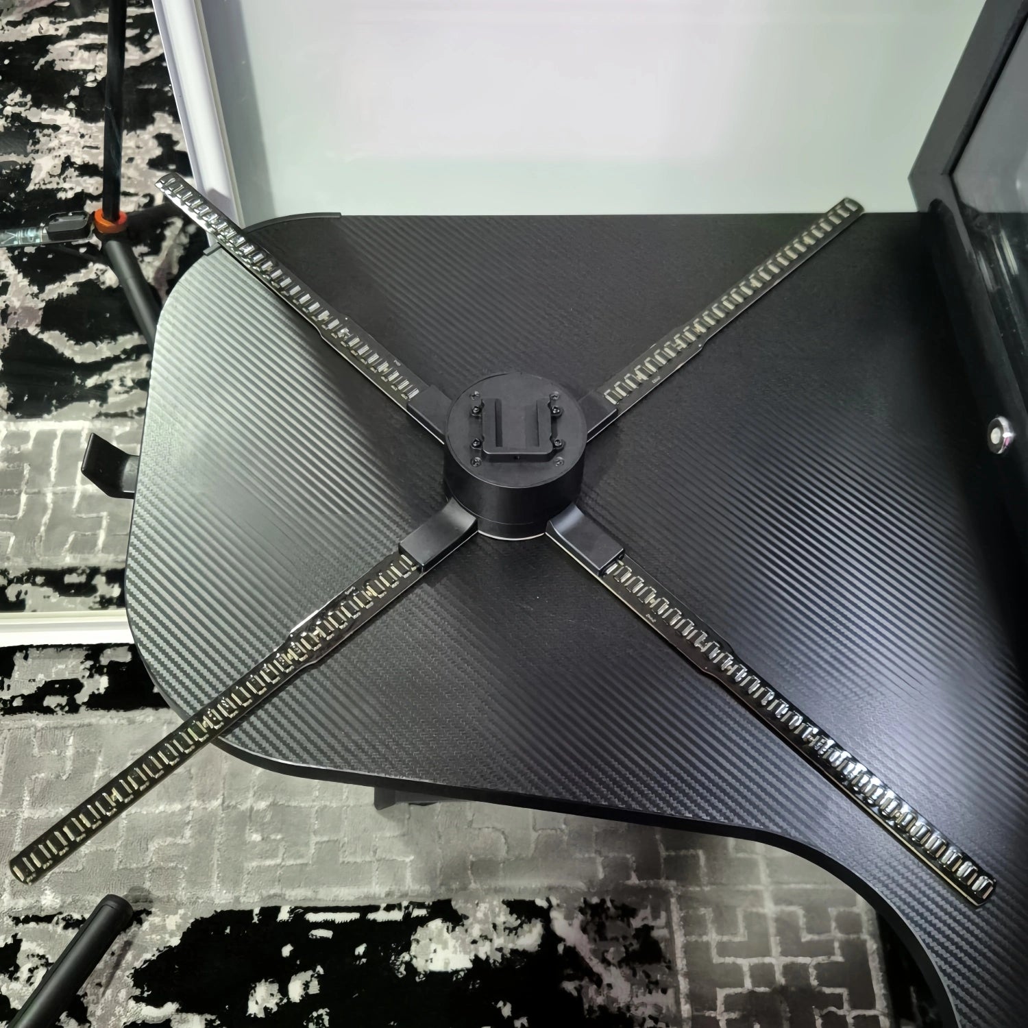 Close-up of the HoloX Ultra 65cm hologram fan showing the four-blade LED rotor on a black textured mounting surface.
