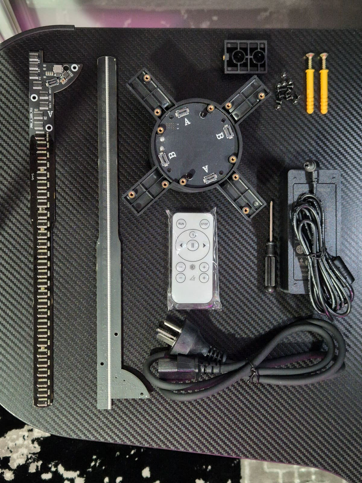 HoloX Ultra 65cm hologram fan components laid out on a carbon-fiber surface.
